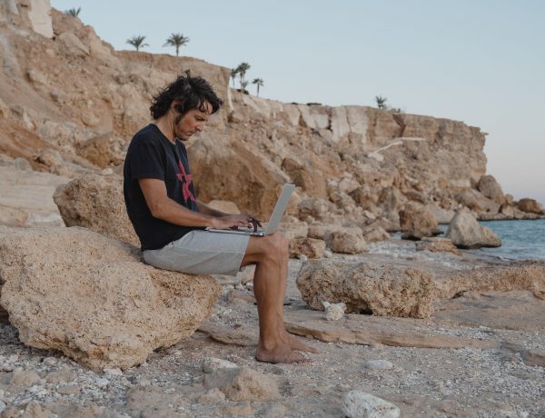 man sitting on a rock while using a laptop